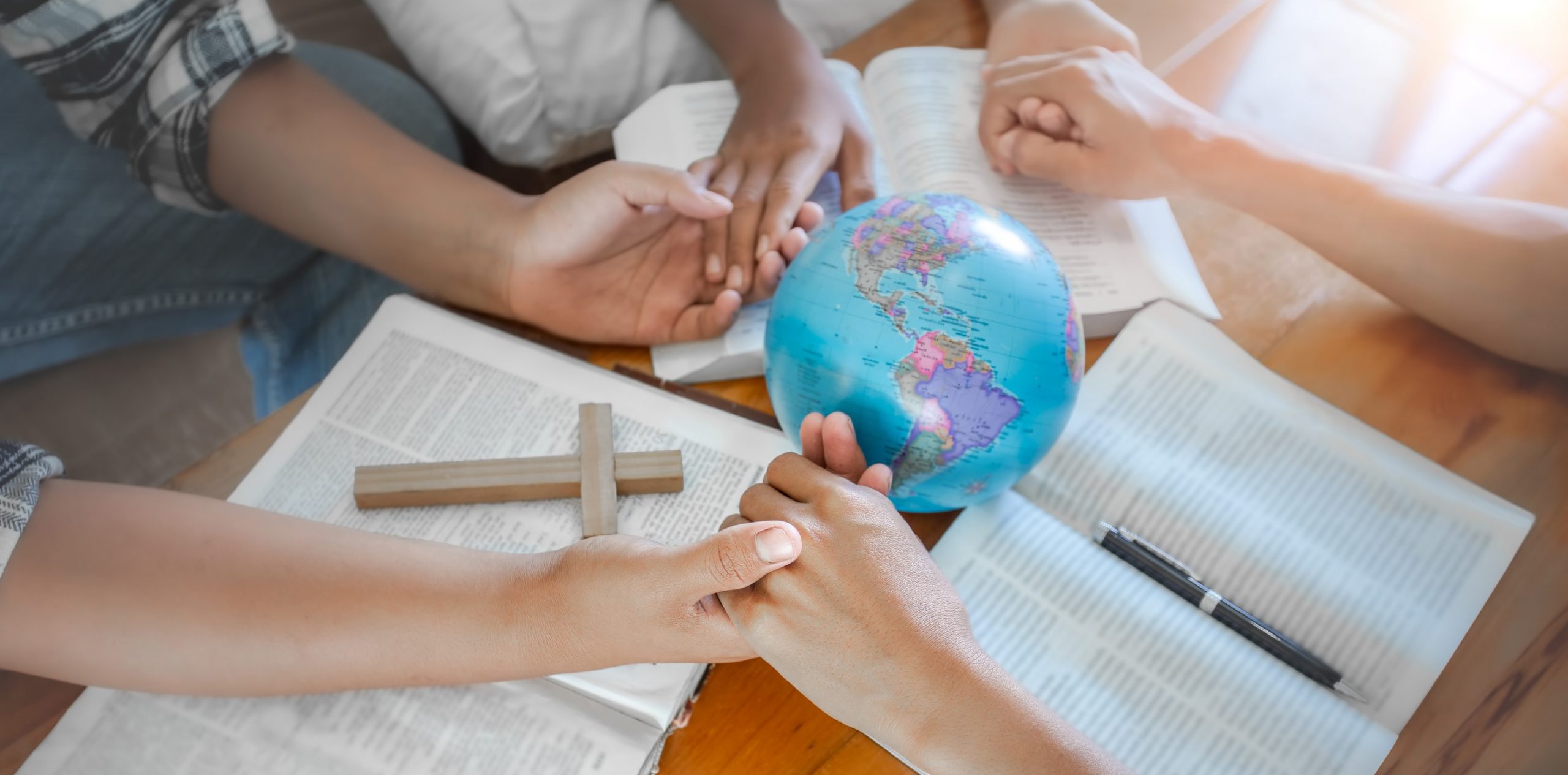 Christian group praying for globe and people around the world on wooden table with bible.